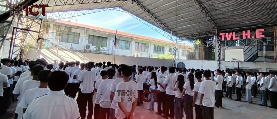 Students in white uniforms stand in morning formation under the Pajo campus gym roof.